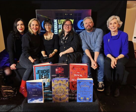 Six people sitting on a sofa with a display of books in the foreground.