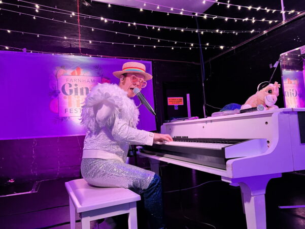 Man dressed in a white sparkly outfit playing a white grand piano.