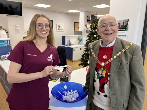 Smiling female in nurse's tunic and the Mayor draw a name from a blue bowl.