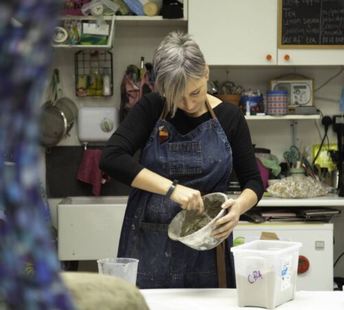 Female artist in a studio stirring a mixture in a bowl.