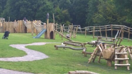 wooden play structure, surrounded by grass, pathway in middle.