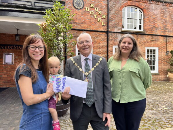 Female holding a baby is presented with an envelope by Mayor and a female wearing a green blouse.