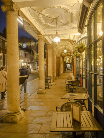 A covered pathway attached to a restaurant what has Christmas lights on the ceiling