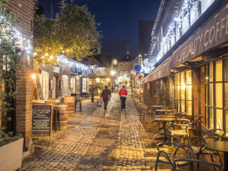 A cobbled street with shops and cafes either side and Christmas lights decorated on the building fronts