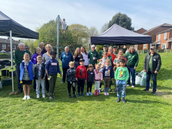 Group of children and adults standing on a grassy area with gazebos in the background.
