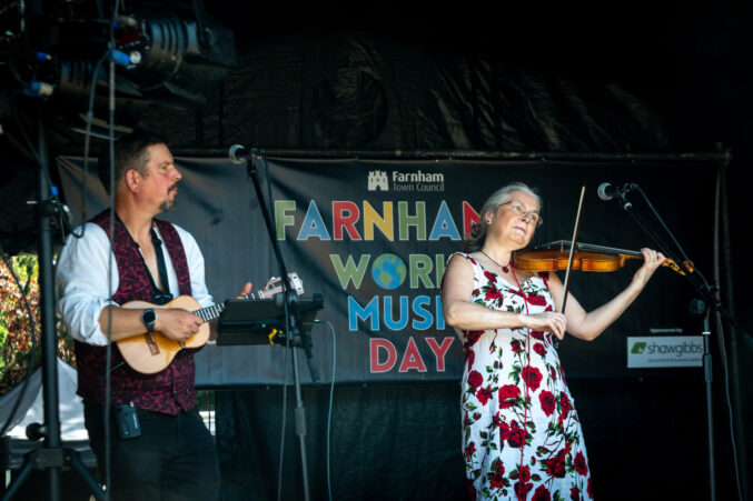 Man playing a banjo and a woman playing a fiddle on a stage.