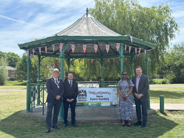 Four people standing either side of a banner attached to a band stand.