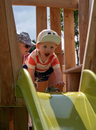 Excited toddler at the top of a yellow baby slide.