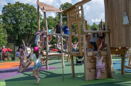 Children climbing, playing and balancing on wooden play equipment.