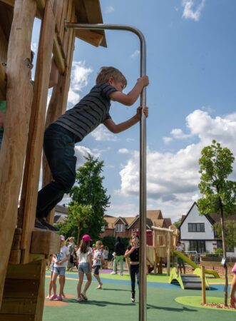 Boy prepares to slide down a fireman's pole in a playground.