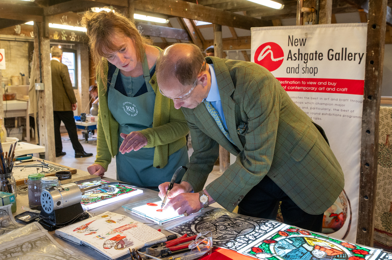 The Duke of Edinburgh uses a tool to cut glass for a stained glass window.